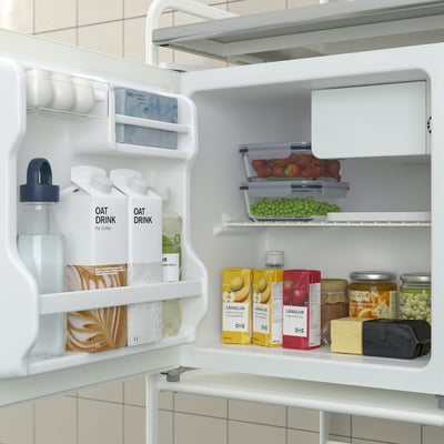 Open fridge with oat drinks, fruit, juice, and storage containers. Shelf and door compartments visible.