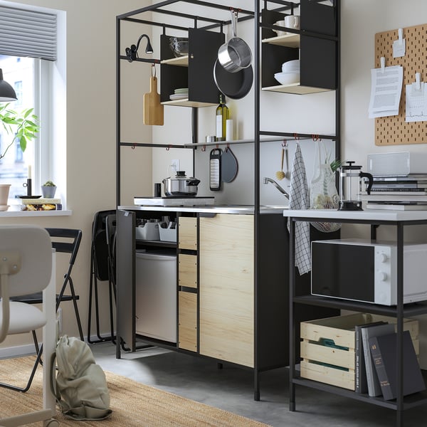 Modern kitchen with black metal shelves, wooden countertop, pots, dishes, microwave, and chairs.