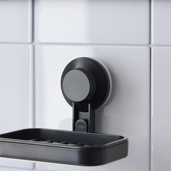 Black soap dish holder with suction cup mounted on tiled wall. Easy to attach and remove, keeps bathroom clean.