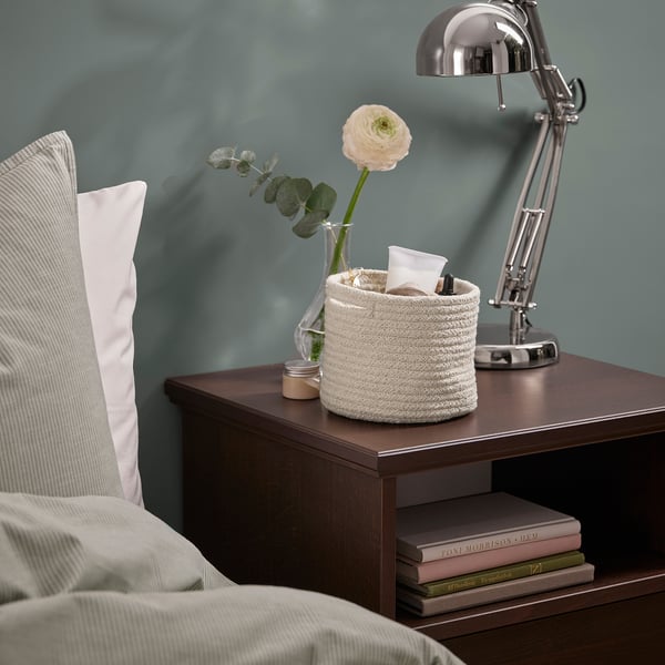 Bedside table with lamp, flowers, basket, and books.
