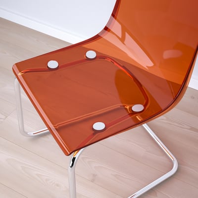 Modern orange transparent chair with chrome legs, sleek design, flexible seat, on light wood floor.