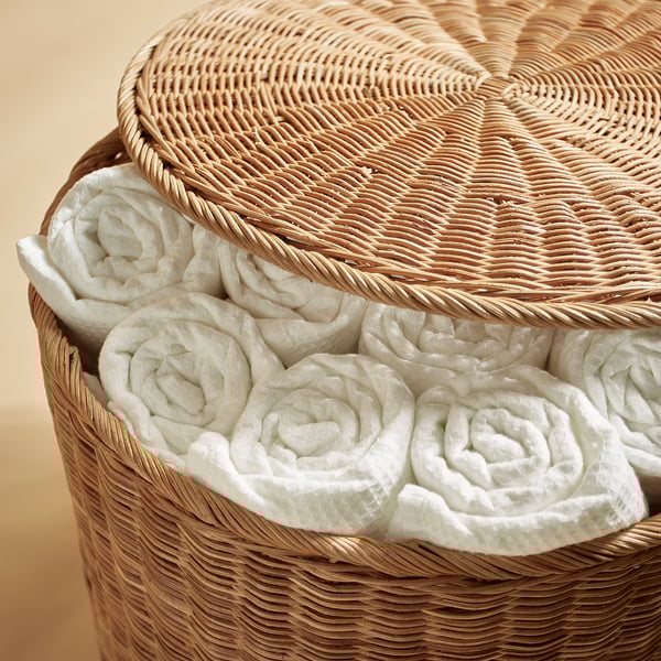 Basket woven from natural rattan, filled with neatly rolled white towels, showcasing quality craft and storage solution.