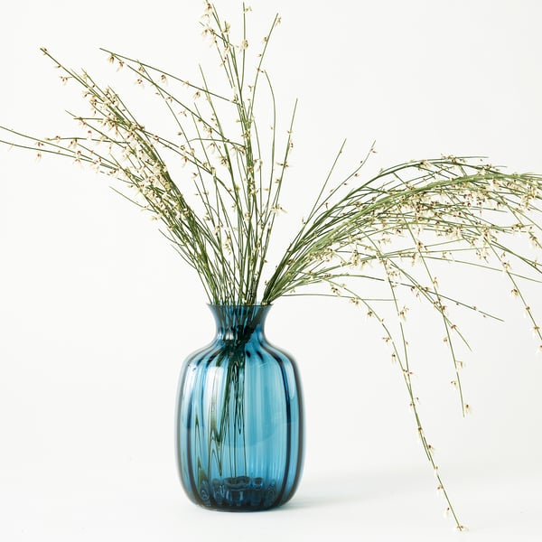 Blue glass vase with green stems and dry flowers, elegant and simple design.