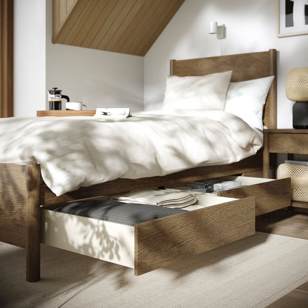 Wooden bed with open drawer showing linens, made with white sheets, coffee tray on top, soft-close storage.