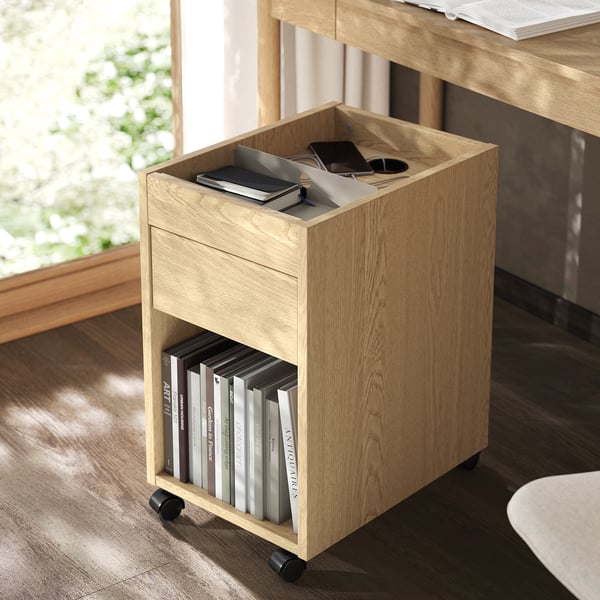 Light wood mobile storage with drawer, holding books and items, under desk.