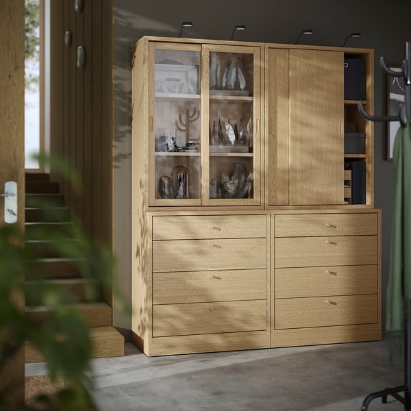 Wooden TONSTAD cabinet with drawers & glass doors, standing tall by stairs, modern-classic design.