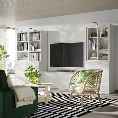 Modern minimalist living room with white TONSTAD tv bench, wicker chair, black-and-white rug, green plants, and built-in bookshelves.
