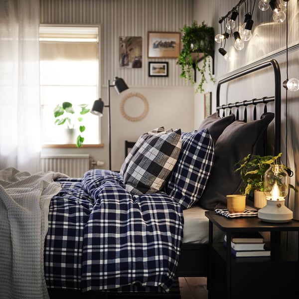 Cosy bedroom with blue chequered bed, bedside table, and plants.