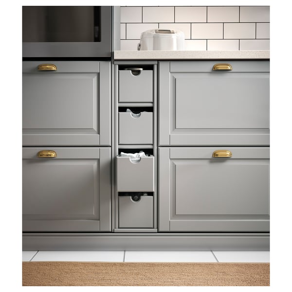Modern grey kitchen cabinets with gold handles, including a pull-out storage box. The countertop a white appliance against a tiled backsplash.