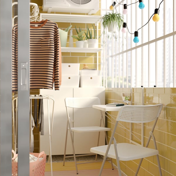 Modern indoor balcony with white TORPARÖ chair, striped shirt, plants, and string lights.