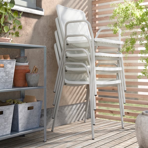 Three stacked white torparo dining chairs on a wooden patio. Shelves with pots and tools on the left, wooden slatted wall on the right.