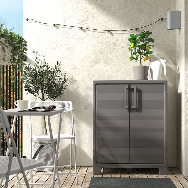 Modern outdoor space: small grey cabinet, white stool, potted lemon tree, string lights.