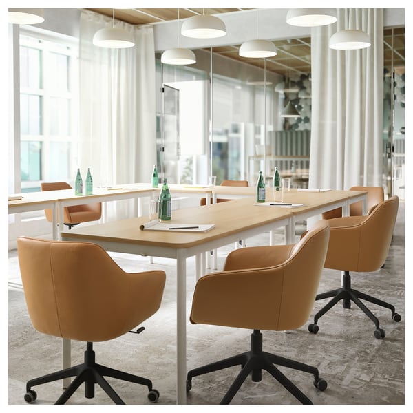 Modern conference room with long wooden table, tan leather swivel chairs, and overhead lighting.