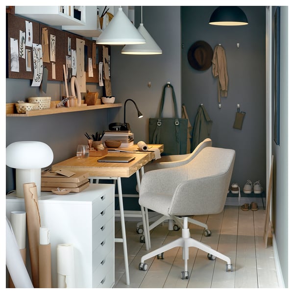 Office corner with TOSSBERG grey swivel chair, wooden desk, pendant lamps, and storage shelves against dark grey wall.