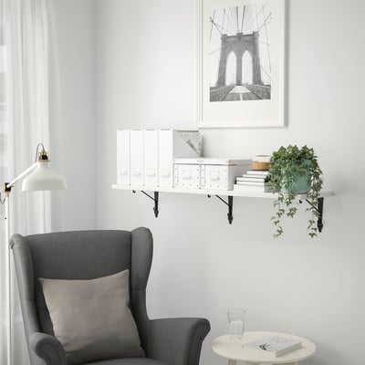 Cosy nook with TRANHULT shelf, books, plant, and armchair. Brooklyn bridge print above, minimalist decor.