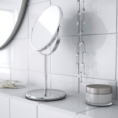 A sleek, tabletop vanity mirror with a base, featuring a magnifying side and a regular reflective side, ideal for makeup or shaving.