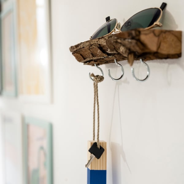 Sunglasses hooked on rustic wooden shelf, below a keychain dangling from a hook.