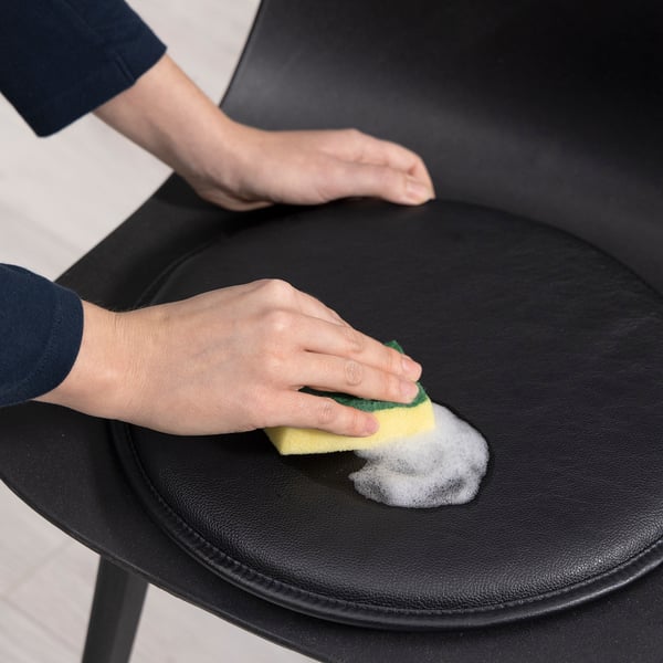 A person cleans a black leather chair with a soapy sponge, demonstrating the TRIXIG leather cleaners ability to clean and maintain leather furniture.