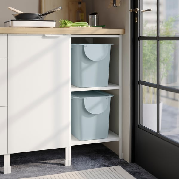 Two light blue TRÖSKNING bins stored in white cabinet, ideal for waste sorting and decor.