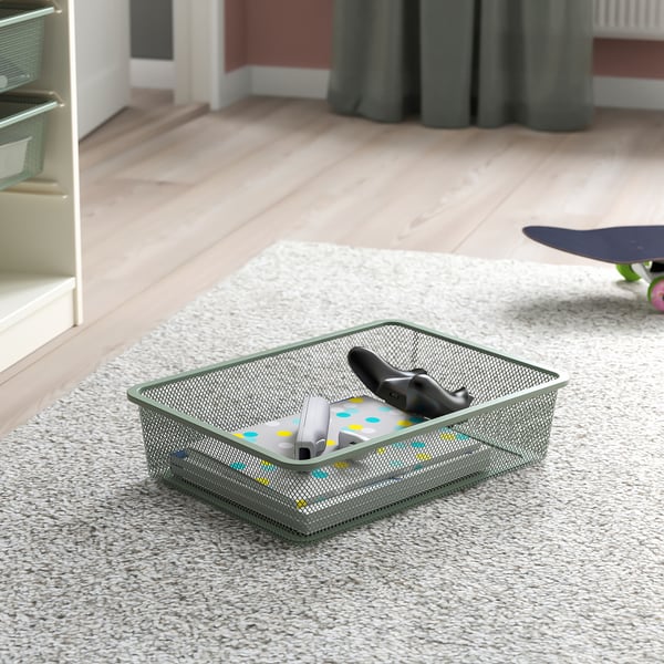 Metal mesh storage box on beige carpet, containing gaming controllers and a remote, perfect for organising gadgets in a TROFAST frame.