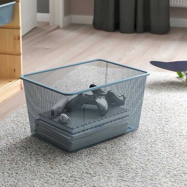 Mesh storage basket on floor, holding small items, part of TROFAST series for organising belongings.