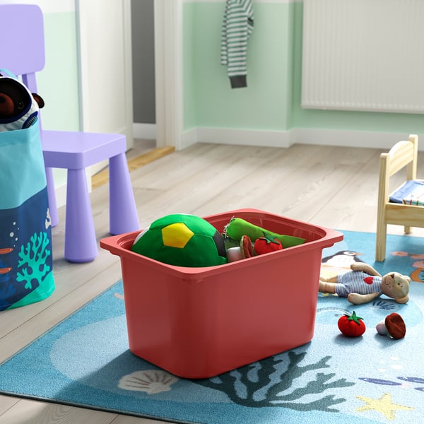 Red TROFAST storage bin filled with green toys on a blue rug in a kids room.