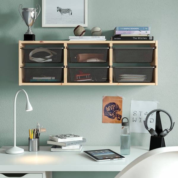 Wall-mounted TROFAST shelf with light wood tone and mesh storage boxes above white desk with essential items.