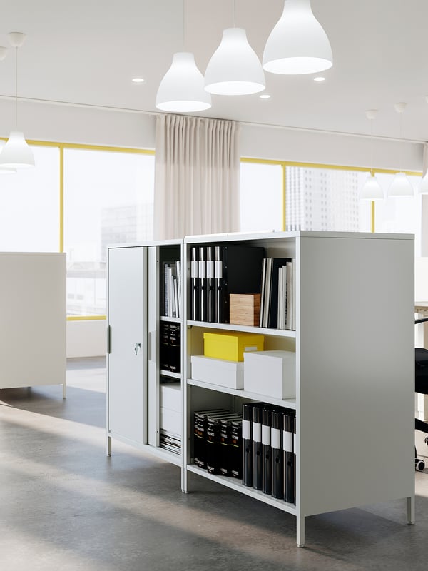 A sleek, silver TROTTEN storage cabinet with sliding doors and shelves in a modern office.