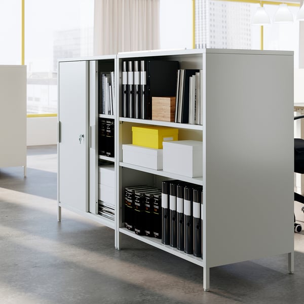 A white trottem double-sided office cabinet with sliding doors, divided into sections. It stores files, binders, and boxes, perfect as a room divider.