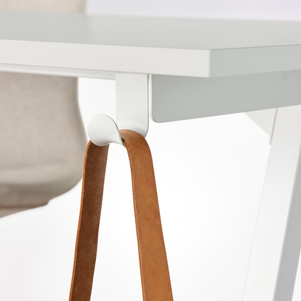 Trottén desk with white hook holding brown leather strap for storage.