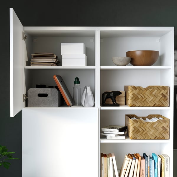 Modern white cabinet, dark green walls. Top: boxes, bowls. Middle: bins, books, decor. Bottom: colourful book stack.