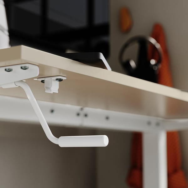 White crank handle on cream desks underside, part of height-adjustable stand-up desk setup.