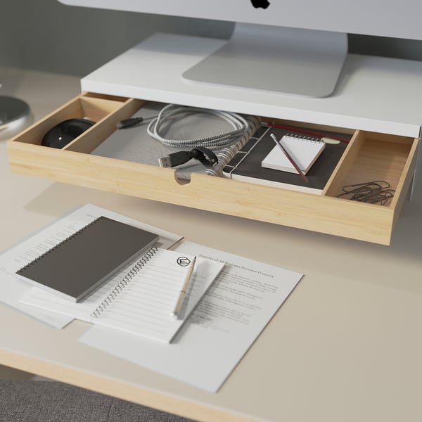 An organised workspace featuring a light-colored wooden desk with a built-in storage drawer containing various office supplies.