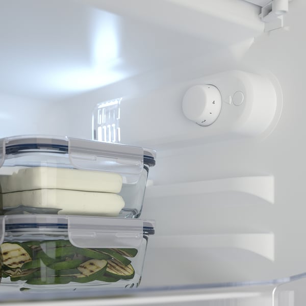 Interior of TYLLSNÄS fridge with full adjustable shelf holding a plastic container with cheese slices, and another container with sliced cucumbers.