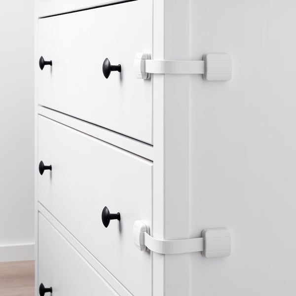 White cabinet with black knobs and two safety latches locking drawers.