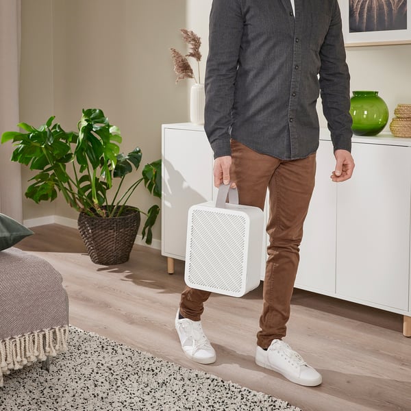 Person carrying portable air purifier through room.