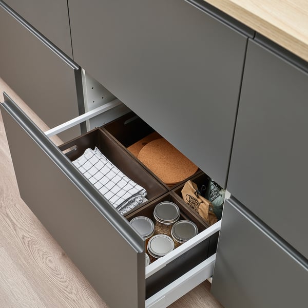 Open kitchen drawer with organised containers and towels. Dark finish, practical storage.