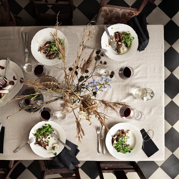 Dinner setup with UPPLAGA plates in white, featuring dishes, cutlery, glasses, and dried flowers.
