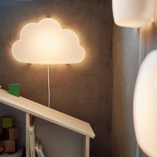Cloud-shaped UPPLYST light fixture on wall, illuminating books and toys with warm glow.
