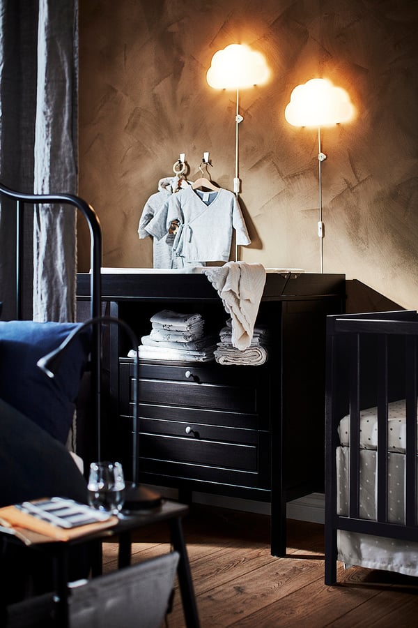 Nursery with black furniture, cloud lamps, grey walls, blue blanket, towels.