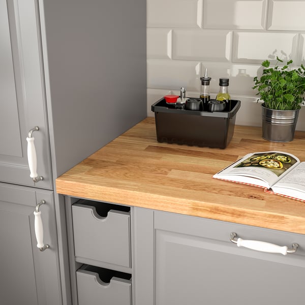 Kitchen counter with cookbook, spice organisers, and herb. Cabinets with white handles.