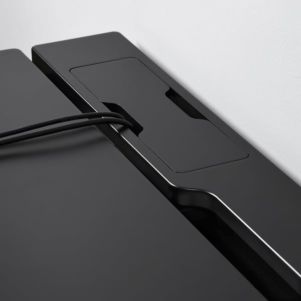 Black desk close-up: sleek, modern design; cable management tray visible; sturdy build quality.