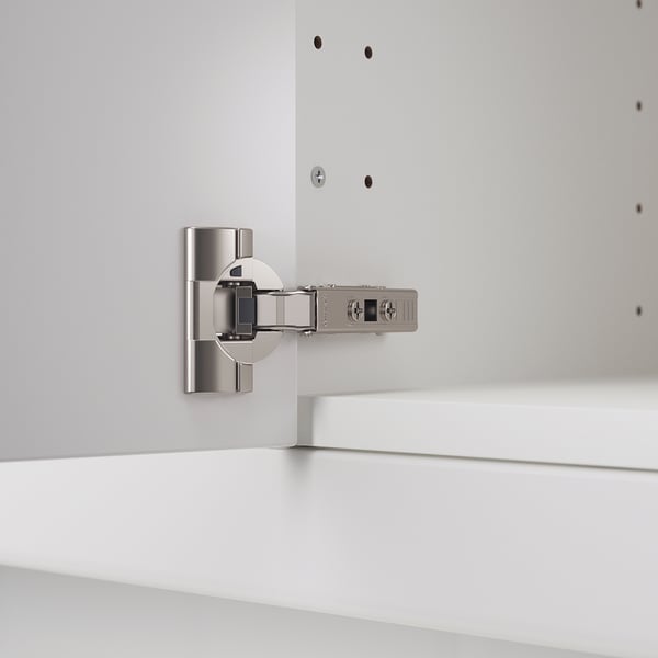Silver kitchen hinge with adjustable arms and integrated damper mounted on white cabinet.
