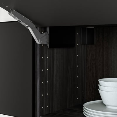 Black kitchen cabinet hinge with damper for soft close, shown partially open. Stacked white bowls and plates inside.
