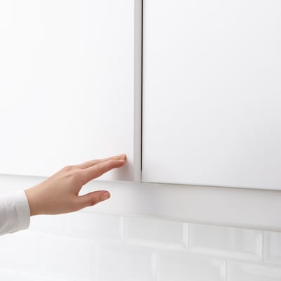Image description: hand pushing a white cabinet door with hidden UTRUSTA push opener.