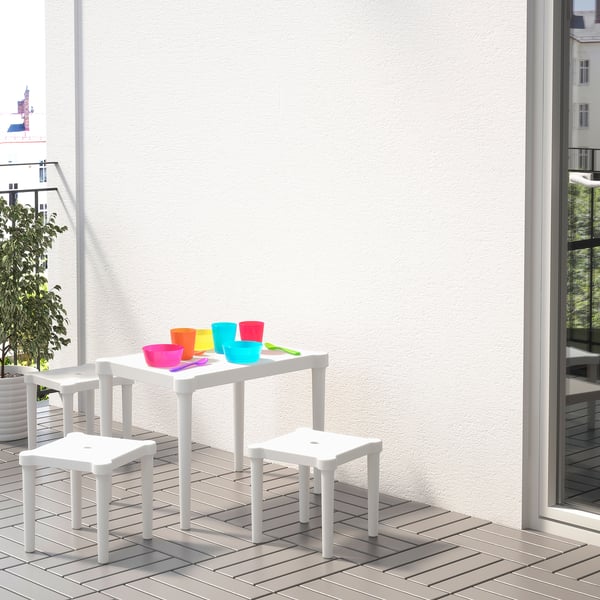 Balustrade, exterior childrens table with colourful cups, white chairs, near window, small tree.