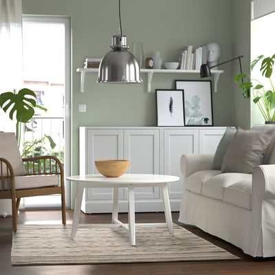 Cosy living room with green walls, white chair, round table, and large traditional rug.