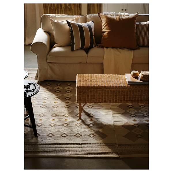 Bright living room with beige sofa, patterned rug, wooden table, and pillows.