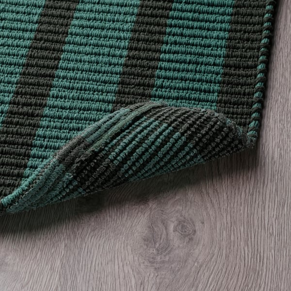 Green and black striped door mat lies on wooden floor, shows anti-slip backing.