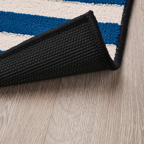 Blue and black striped rug with black non-slip backing on wooden floor.